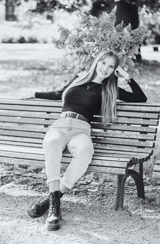 A cheerful woman sitting on a wooden bench outdoors, captured in black and white.